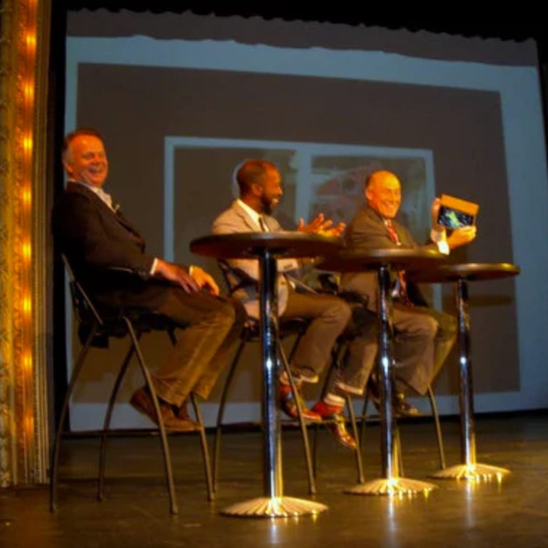 Local celebrity contestants laughing at game-show tables on stage